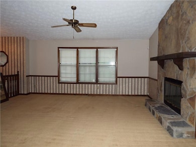 Unfurnished living room with a textured ceiling, a ceiling fan, carpet floors, wallpapered walls, and a stone fireplace