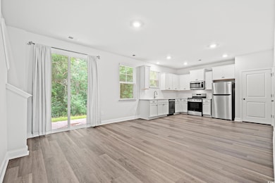 Kitchen with appliances with stainless steel finishes, light wood finished floors, light countertops, white cabinets, and recessed lighting