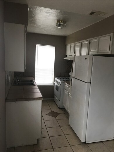 Kitchen featuring white cabinets, white refrigerator, light tile patterned flooring, range, and extractor fan