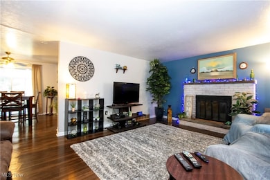 Living room featuring dark wood-style flooring, a brick fireplace, and ceiling fan