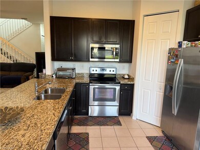Kitchen with appliances with stainless steel finishes, light stone countertops, light tile patterned floors, open floor plan, and dark brown cabinets