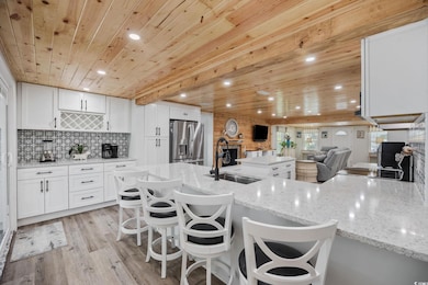 Kitchen with white cabinetry, wood ceiling, stainless steel refrigerator with ice dispenser, light stone countertops, and light wood-style floors
