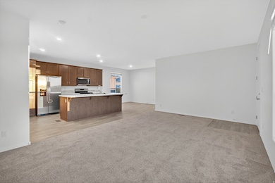 Kitchen with open floor plan, light colored carpet, light countertops, appliances with stainless steel finishes, and an island with sink
