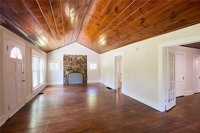 Unfurnished living room featuring vaulted ceiling, dark wood-style floors, a stone fireplace, wooden walls, and wood ceiling