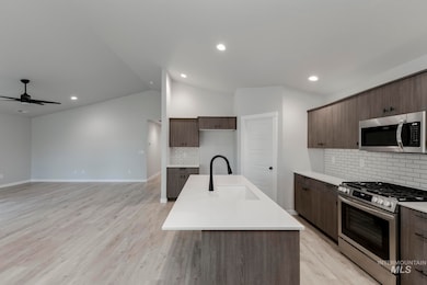 Kitchen with stainless steel appliances, tasteful backsplash, a center island with sink, light wood-style flooring, and lofted ceiling