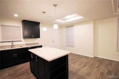 Kitchen featuring dark cabinetry, hanging light fixtures, dark wood-style floors, a kitchen island, and open shelves