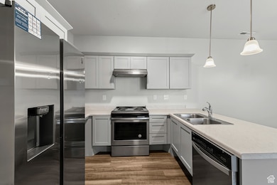 Kitchen featuring stainless steel appliances, a peninsula, light countertops, dark wood finished floors, and hanging light fixtures