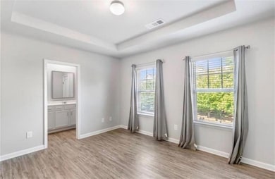 Unfurnished bedroom with a raised ceiling, light wood-style flooring, and ensuite bathroom