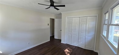 Unfurnished bedroom featuring ornamental molding, dark wood finished floors, a closet, and ceiling fan