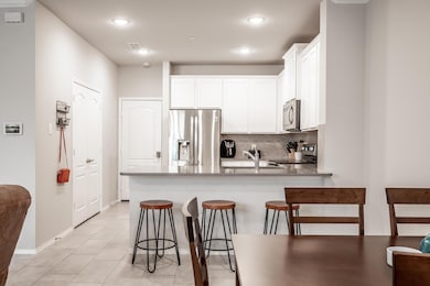 Kitchen featuring stainless steel appliances, a kitchen breakfast bar, backsplash, white cabinetry, and light tile floors
