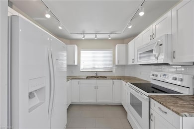 Kitchen featuring white appliances, granite countertops, track lighting, and white cabinetry
