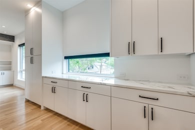 Kitchen with white cabinetry, light wood-type flooring, modern cabinets, light stone countertops, and recessed lighting