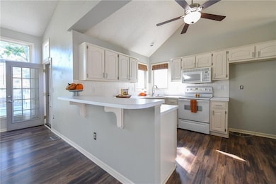 Kitchen with backsplash, a breakfast bar area, light countertops, white appliances, and a peninsula
