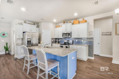 Kitchen featuring decorative backsplash, white cabinets, light stone counters, a kitchen bar, and recessed lighting