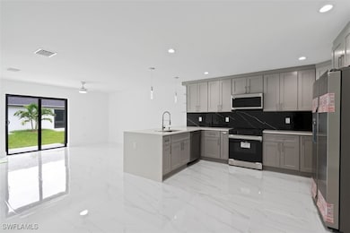 Kitchen with gray cabinetry, stainless steel appliances, a peninsula, backsplash, and light marble finish flooring