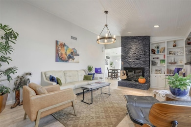Living room with vaulted ceiling, light wood-style floors, a stone fireplace, and built in features