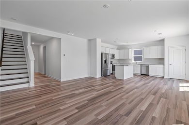 Unfurnished living room featuring light wood-type flooring, baseboards, stairway, a sink, and recessed lighting