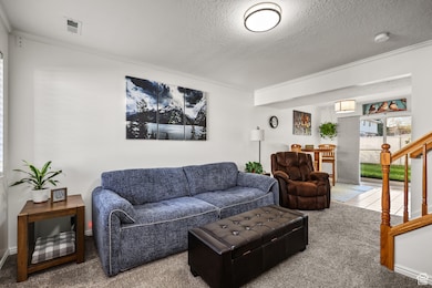 Carpeted living room featuring a textured ceiling, stairs, and ornamental molding