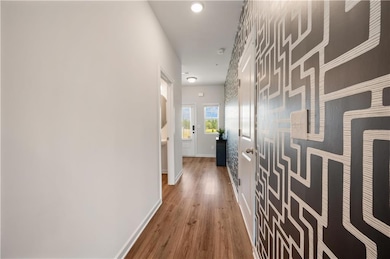 Corridor with wallpapered walls, light wood-type flooring, an accent wall, and recessed lighting