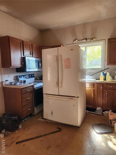 Kitchen featuring tasteful backsplash, freestanding refrigerator, light countertops, stainless steel range oven, and brown cabinets