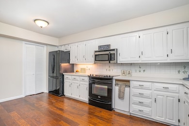 Kitchen featuring light countertops, backsplash, white cabinets, black appliances, and dark wood-style flooring