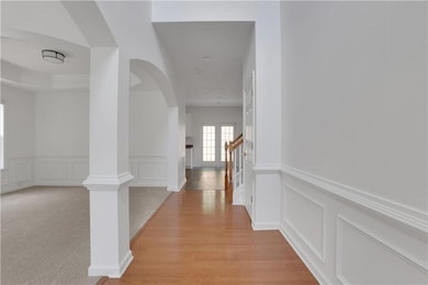 Hallway featuring arched walkways, a decorative wall, a wainscoted wall, ornate columns, and light wood-style flooring