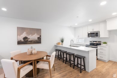 Kitchen featuring appliances with stainless steel finishes, recessed lighting, a breakfast bar area, light wood-style floors, and white cabinetry