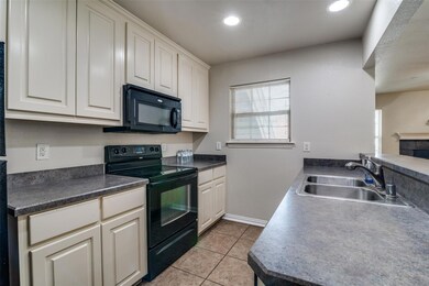 Kitchen featuring sink, white cabinetry, light tile flooring, and black appliances