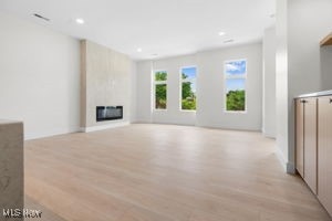 Unfurnished living room featuring light wood-type flooring, a large fireplace, recessed lighting, and radiator heating unit