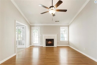Unfurnished living room featuring wood finished floors, a ceiling fan, a fireplace, crown molding, and baseboards