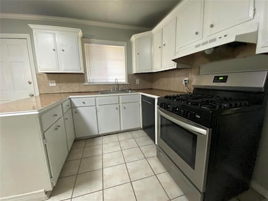 Kitchen with gas stove, under cabinet range hood, tasteful backsplash, white cabinets, and crown molding