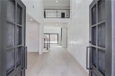 Entryway featuring a decorative wall, a towering ceiling, light wood-style floors, recessed lighting, and stairs