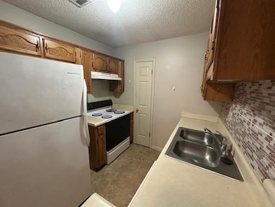 Kitchen with white appliances, light countertops, decorative backsplash, a textured ceiling, and under cabinet range hood