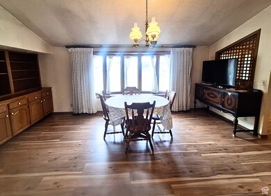 Dining room featuring a textured ceiling, a chandelier, dark wood-type flooring, and vaulted ceiling