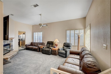 Carpeted living area with ceiling fan, a stone fireplace, and a textured wall