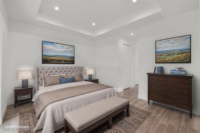Bedroom featuring a raised ceiling, light wood-style floors, recessed lighting, and baseboards