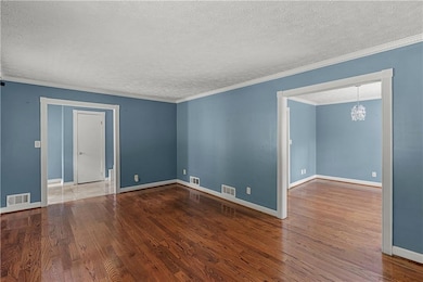 Empty room featuring a textured ceiling, dark wood finished floors, ornamental molding, and a chandelier