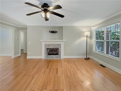 Unfurnished living room with ornamental molding, light wood finished floors, a fireplace, and a ceiling fan