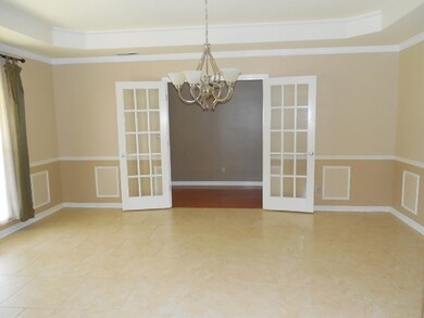 The formal dining room opens off the foyer with French doors and features high trey detail ceilings, crown molding, and tile floors.