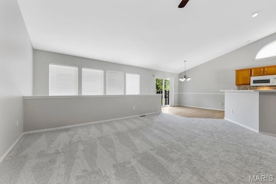 Unfurnished living room featuring light carpet, lofted ceiling, ceiling fan, and a chandelier