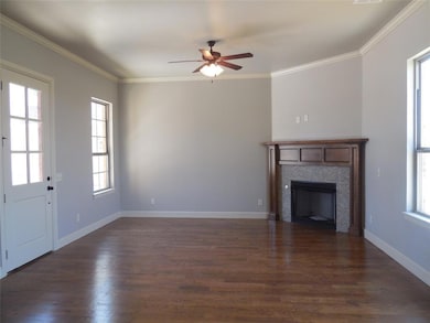 Unfurnished living room with plenty of natural light, dark wood-style floors, ornamental molding, a ceiling fan, and a tile fireplace
