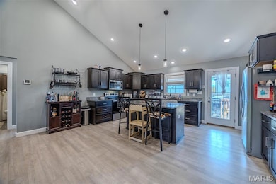 Kitchen with a kitchen breakfast bar, hanging light fixtures, a kitchen island, appliances with stainless steel finishes, and dark stone counters