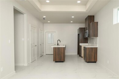 Kitchen featuring stainless steel microwave, baseboards, light countertops, recessed lighting, and a kitchen island with sink