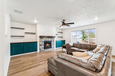 Living room featuring a stone fireplace, light wood-type flooring, ceiling fan, a textured ceiling, and recessed lighting