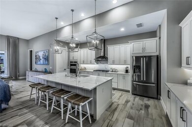 Kitchen with stainless steel appliances, a breakfast bar area, pendant lighting, light stone countertops, and an island with sink