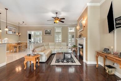 Living room with ceiling fan, a glass covered fireplace, wood finished floors, and ornamental molding