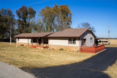 Ranch-style house featuring stone siding, a deck, a shingled roof, and a front lawn