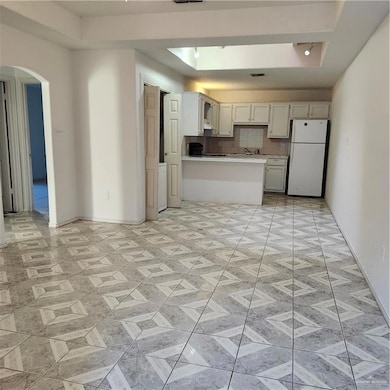 Kitchen with arched walkways, decorative backsplash, fridge, light countertops, and a peninsula