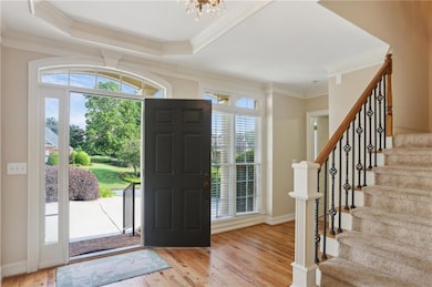 Entrance foyer with stairs, light wood-style flooring, a chandelier, crown molding, and a tray ceiling