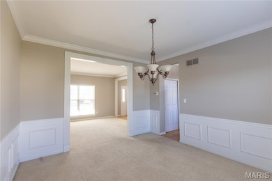 Spare room with wainscoting, a decorative wall, light colored carpet, crown molding, and a chandelier